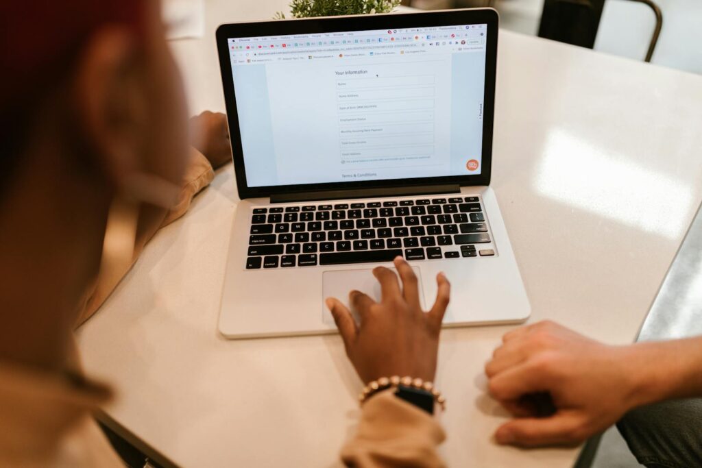 Two adults working together on a laptop displaying an online form, indoors.